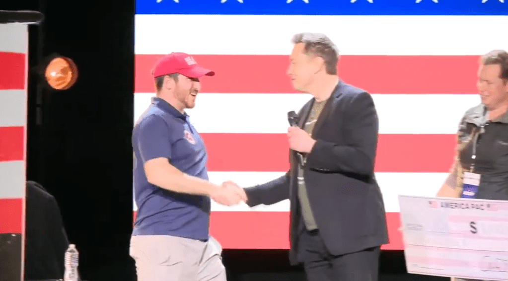 Musk shakes hands with an over-sized million dollar check from Musk.